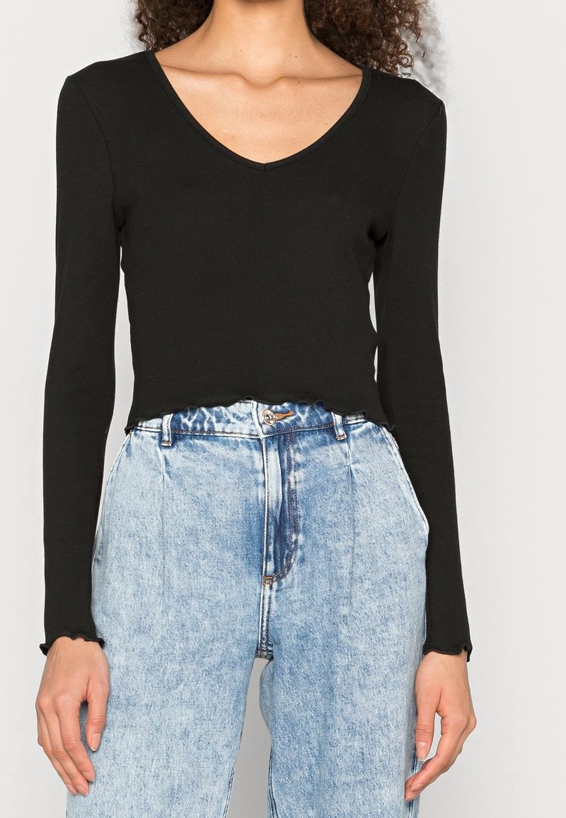 Haut noir à manches longues avec un décolleté en V et une texture côtelée, associé à un jean clair taille haute avec une coupe décontractée et un motif décoloré.
