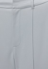 Pantalon gris clair ajusté montrant la ceinture, les passants de ceinture, la couture avant et une texture de tissu subtile.