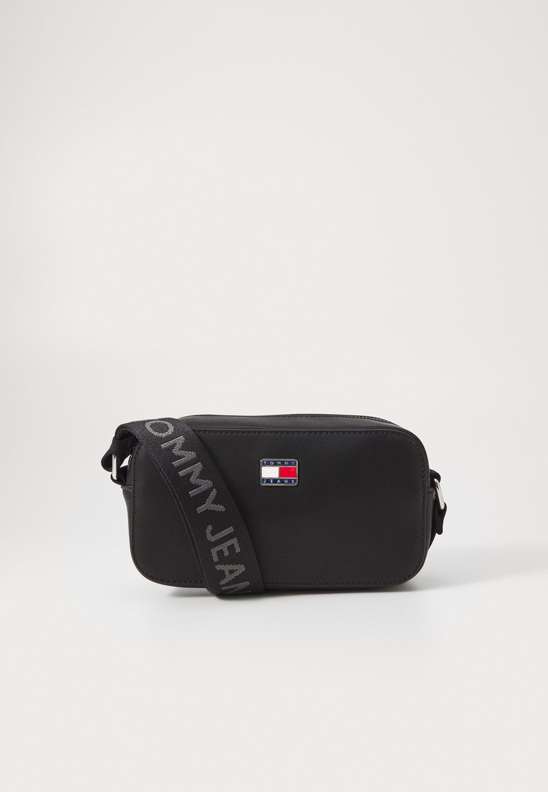 Černá obdélníková crossbody taška vyrobená z hladkého materiálu s nastavitelným popruhem. Obsahuje malou nášivku s logem a text na popruhu.