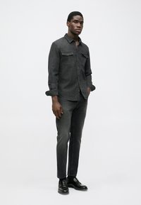 Dark grey denim shirt with buttoned front, two chest pockets, and rolled sleeves. Paired with dark grey slim-fit jeans and black shoes.