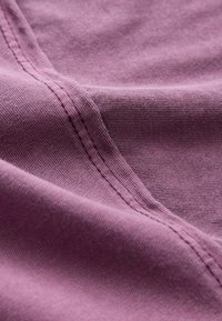 Textil tyg i dämpad lila, med en mjuk, texturerad yta och synlig sömnad längs kanterna, vilket ger en slät och flödande känsla.