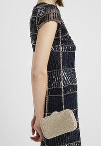 Borsa clutch metallizzata con superficie dorata texturizzata, forma rettangolare, decorata con piccoli strass e tracolla a catena argentata.