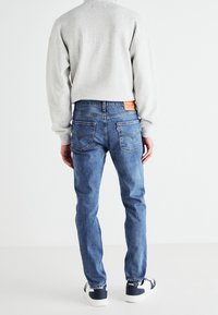 Sudadera gris y jeans de mezclilla azul combinados con zapatillas blancas y marinas. Los jeans tienen bolsillos traseros y una etiqueta de cuero beige en la cintura.