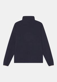 Námořnický pulovr s vysokým límcem, dlouhými rukávy a volným střihem. Na rukávu je malý logo detail. Hladká textura.