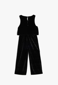 Svart sammets jumpsuit med ärmlös topp och rundad hals, i en kort design, ihopparad med vida byxor.