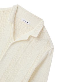 Camicia bianca a maglia con bottoni, caratterizzata da un motivo testurizzato con diverse trame aperte, colletto classico e etichetta con la scritta "Terranova XL."
