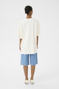 Overmaat crème t-shirt met verlaagde schouders, gecombineerd met mid-blue denim shorts. Witte puntige schoenen maken de outfit af.