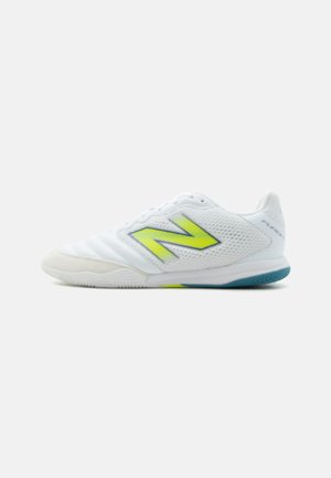 Witte sportschoen met een neon geel "N" logo, ademende mesh-zijden en een blauw-witte rubberen zool, getoond in profiel.