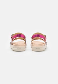 Sandales métalliques violettes avec une sangle à boucle, semelle intérieure beige matelassée et semelle extérieure en caoutchouc blanche, montrant une vue arrière élégante.