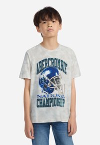 Īsām piedurknēm, gaiši pelēks krāsu apvienojuma T-krekls ar zilu futbola ķiveres grafiku un bolderiem "Abercrombie NACIONĀLĀ ČEMPIONĀTA".