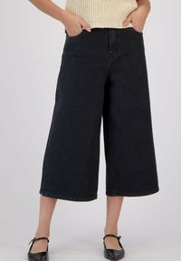Des culottes à jambes larges en denim noir avec une taille haute, des poches latérales et une coupe droite, complétant un top en tricot léger et des chaussures plate.