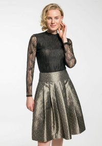 Schwarzes Spitzenoberteil mit langen Ärmeln, kombiniert mit einem metallic gefalteten Rock, der komplizierte Muster in Gold- und Silbertönen aufweist.