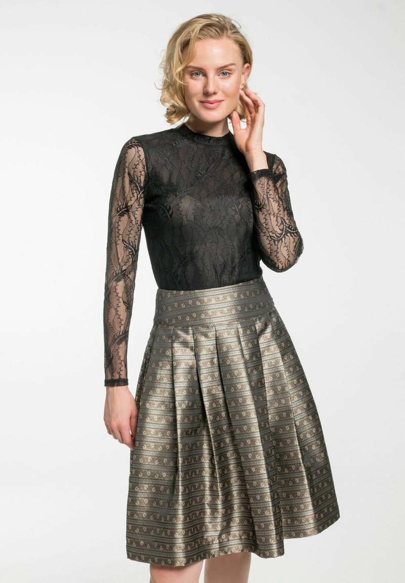 Schwarzes Spitzenoberteil mit langen Ärmeln, kombiniert mit einem metallic gefalteten Rock, der komplizierte Muster in Gold- und Silbertönen aufweist.