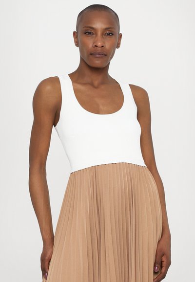 Top in cotone bianco a costine con scollatura a girocollo, abbinato a una gonna beige plissettata. Il vestito presenta una transizione di tessuto a contrasto in vita.
