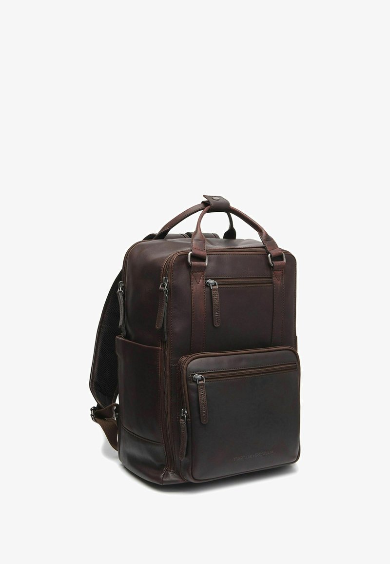 Sac à dos en cuir marron avec plusieurs poches zippées, une poignée supérieure et des bretelles rembourrées. Présente une texture lisse et un design structuré.