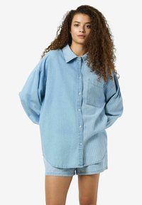 Chemise en denim bleu clair surdimensionnée avec un design à rayures, fermeture à boutons, et une poche poitrine unique ; associée à un short à rayures assorti.