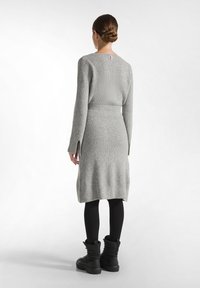 Graues gestricktes Kleid mit taillierter Taille, langen Ärmeln, seitlichen Schlitzen und einem runden Ausschnitt, kombiniert mit schwarzen knöchellangen Stiefeln.