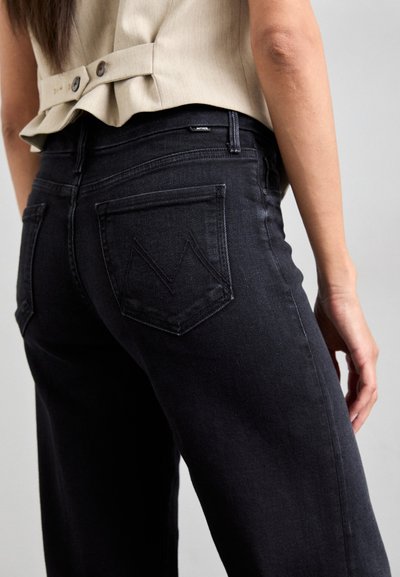Black denim jeans featuring a standard back pocket design with a chevron pattern. Fabric is soft with a slight sheen, tailored for a relaxed fit.