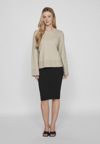 Smėlinis mezginiu megztinis su apykakle ir ilgomis rankovėmis, derinamas su prisitaikančia juoda pieštuko sijonu ir juodais skaidriais šlepetėmis.