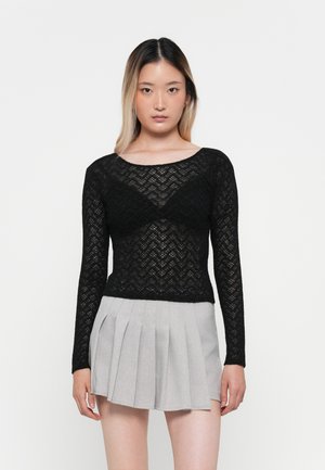 Haut noir en dentelle à manches longues avec un motif en zigzag et une texture transparente, associé à une mini-jupe plissée gris clair.