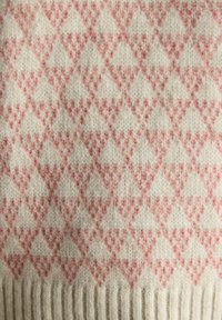 Gestickter Stoff mit sich wiederholendem Muster aus kleinen rosa geometrischen Herzformen auf einem cremigen Hintergrund, mit geripptem Saum am unteren Rand.