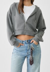 Grijze korte zip-up hoodie met capuchon, lange mouwen en een voorzak, gecombineerd met hoge taille vervaagde blauwe denim jeans.