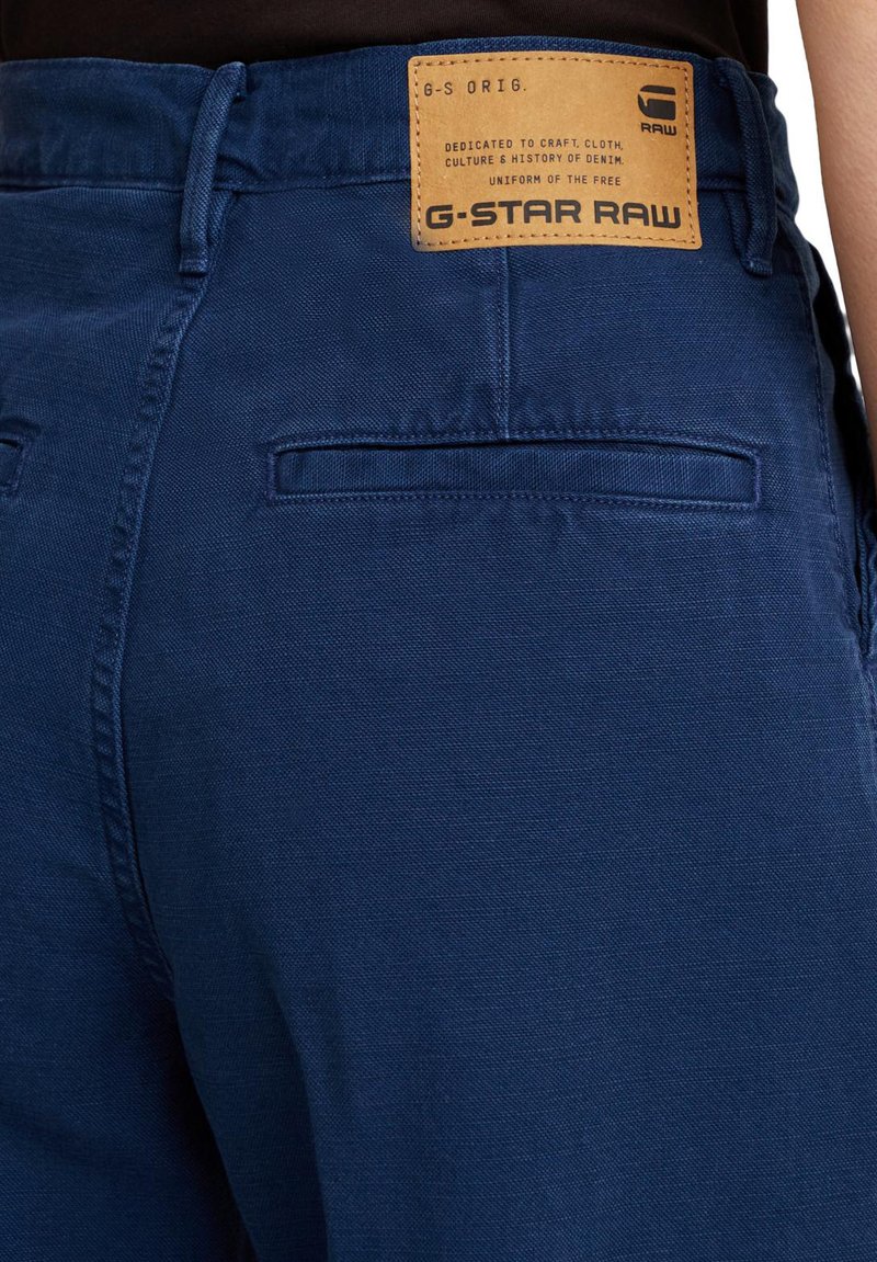 Niebieskie dżinsowe spodnie z tkaną fakturą, detalami tylnych kieszeni oraz brązową skórzaną metką z wytłoczonym napisem "G-Star RAW".
