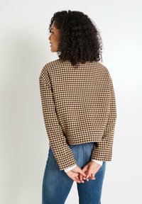 Pull court à motif pied-de-poule marron avec coupe ample, manches longues et poignets blancs, associé à un jean en denim bleu.
