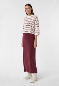 Gestreifter Strickpullover in Weiß, Burgunderrot und Marineblau, kombiniert mit einem burgunderfarbenen Maxikleid. Das Model trägt weiße Ankle Boots mit dicken Sohlen.