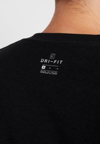 Gros plan sur le tissu noir Dri-FIT au niveau du haut du dos, montrant l'étiquette taille moyenne et le texte « Made in China » sous le logo.