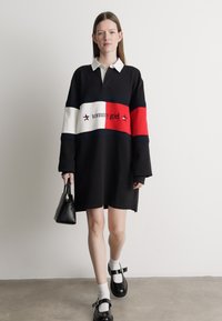 Čierna oversized mikinová šaty s bielym golierom, s červenými a bielymi vodorovnými pruhmi a logom "tommy girl". Nosené s čiernymi topánkami.