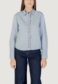 Camicia azzurro chiaro con colletto e bottoniera, decorata con elementi a forma di fiore, e maniche lunghe, abbinata a pantaloni in denim scuro.