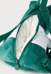 Πράσινο βελούδινο σακίδιο με ρυθμιζόμενους ιμάντες, ανοιχτό φερμουάρ που αποκαλύπτει λευκή υφασμάτινη επένδυση στο εσωτερικό.