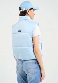 Šviesiai mėlynas pūkų liemuo su aukštu apykakle, ant nugaros yra etiketė. Dėvimas ant baltos marškinėlių ir derinamas su šviesiai mėlynomis džinsinėmis kelnėmis.