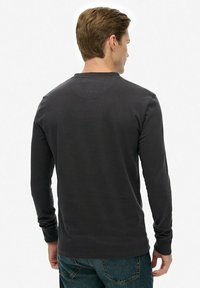 Koszula z długim rękawem w ciemnoszarym kolorze, wykonana z miękkiego materiału, z okrągłym dekoltem i prostym wzorem z tyłu, z minimalną ilością szwów.