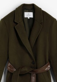 Abrigo de mezcla de lana color verde oliva con cuello de solapa, cierre de un solo botón y un cinturón marrón brillante que acentúa la cintura.