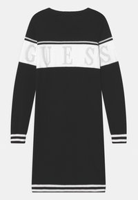 Czarna dzianinowa sukienka z poziomym białym paskiem z napisem "GUESS" w srebrnym kolorze, prążkowanymi mankietami i okrągłym dekoltem.