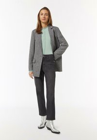 Grau strukturierter Blazer, mintgrünes Oberteil, dunkle Jeans und silberne Stiefeletten. Verfügt über einen einzigen Knopf, gerade Beine und klare Linien.