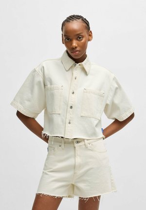 Krótkie, kremowe denimu koszula z krótkimi rękawami, dwiema przednimi kieszeniami, zapięciem na guziki i postrzępionym dołem. W komplecie z pasującymi szortami o wysokim stanie.