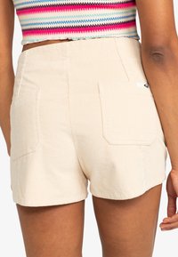 Shorts en velours côtelé beige avec deux poches arrière, une texture subtile et un ourlet arrondi, adaptés pour une tenue décontractée.