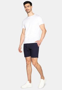 Shorts blu navy con cordoncino, abbinati a una maglietta bianca semplice e sneakers bianche. I pantaloni corti presentano una tasca laterale e una vestibilità casual.