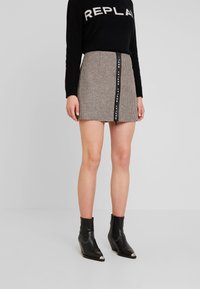 Houndstooth mini rok met een zwarte rits met "REPLAY" branding, gecombineerd met zwarte enkellaarsjes met zilveren accenten.