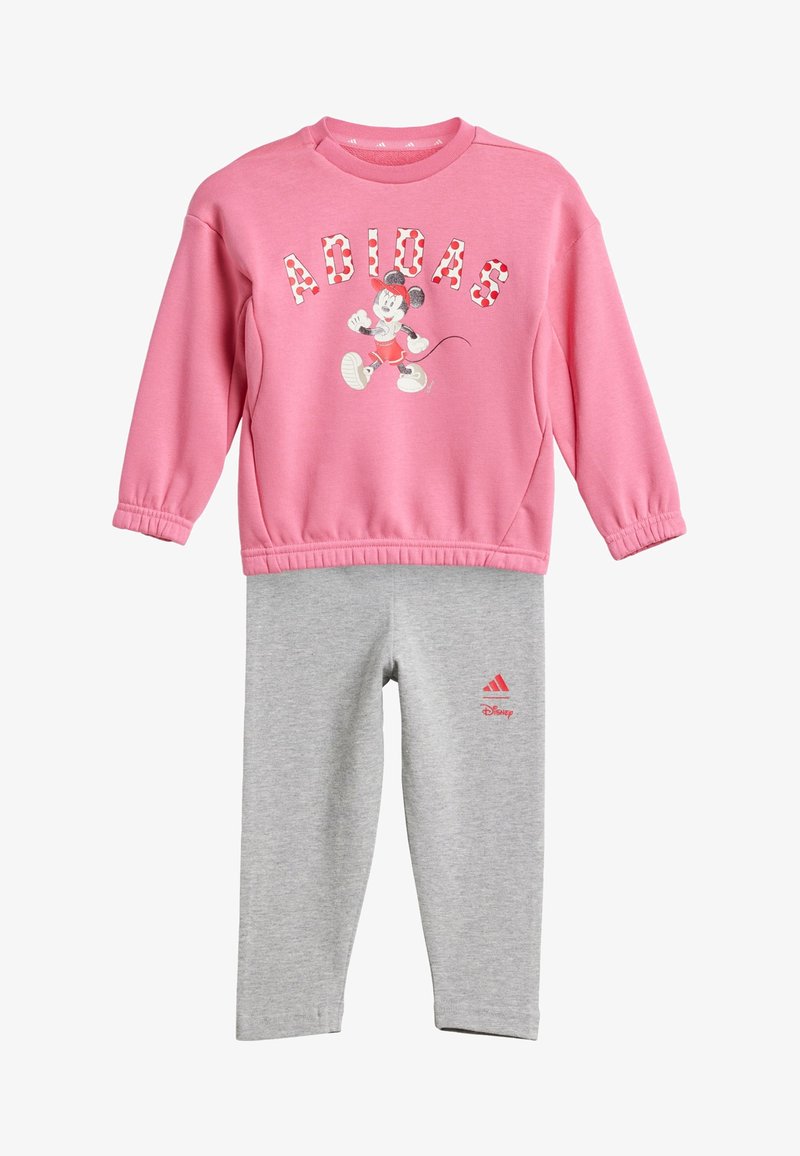 Różowa bluza z białymi i czerwonymi literami "ADIDAS" oraz grafiką Myszki Miki, w połączeniu z szarymi legginsami z czerwonym logo Adidas.