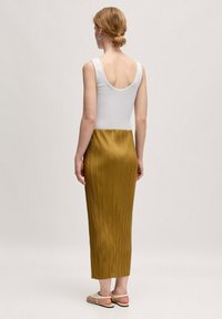 Witte mouwloze top met een ruime ronde achterkant, gecombineerd met een geplooide mosterdgele midi-jurk. De jurk heeft een zachte textuur en een elastische tailleband.