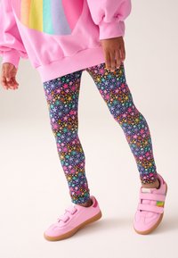 Barvite legice z vzorcem zvezd v rožnati, rumeni, modri in zeleni barvi na temnem ozadju; kombinirane z rožnatim puloverjem in čevlji.