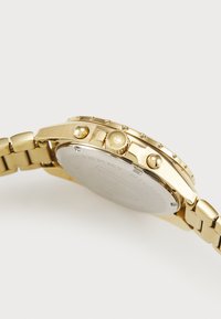 Gullforgan håndleddsklokke med rund kasse, en teksturert bezel og en sammenkoblet metallarmbånd. Hvit skive med minimale merker og tre knapper.