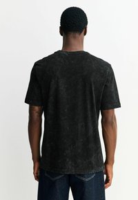 Czarny T-shirt z krótkim rękawem o teksturowanym wykończeniu i okrągłym dekoltem, widziany od tyłu. Charakteryzuje się luźnym krojem i subtelnym wzorem.