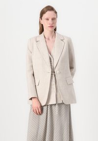 Lysebeige linjakke med klippede rever, enkel knappelukking og to lommer, sammen med et stripete grått skjørt.