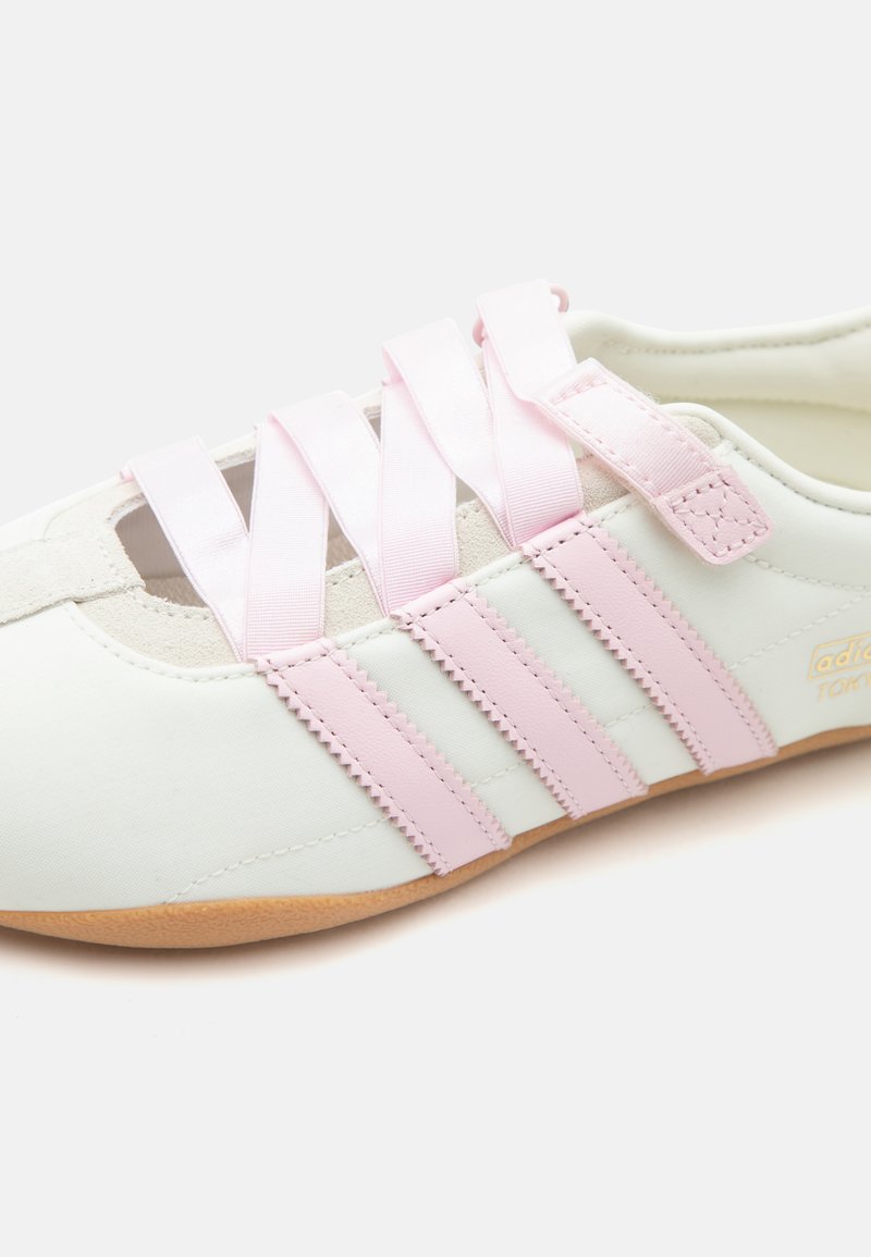 Witte sneaker met lichtroze strepen en brede lintachtige veters, met een gumzool en suède accenten.