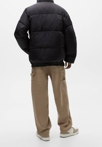 Sort puffet jakke med quiltede sektioner, elastisk talje og høj krave, kombineret med beige cargobukser med sidelommer og en afslappet pasform.